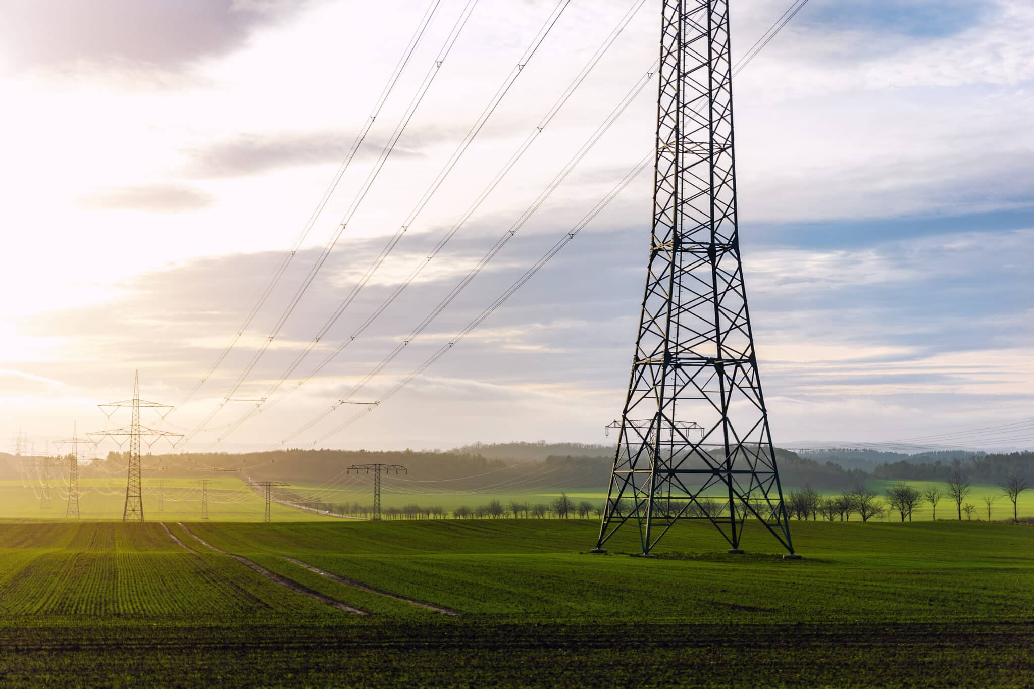 Scenic view of electricity pylons stretching across green fields warm sunset sky background. Electric power supply high voltage metal tower in Europe.